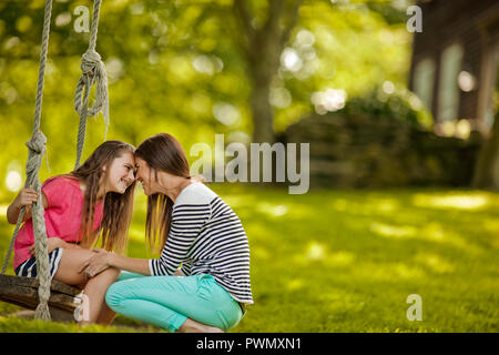 Young girl sitting on a rope swing affectionate nudges her mother. Stock Photo