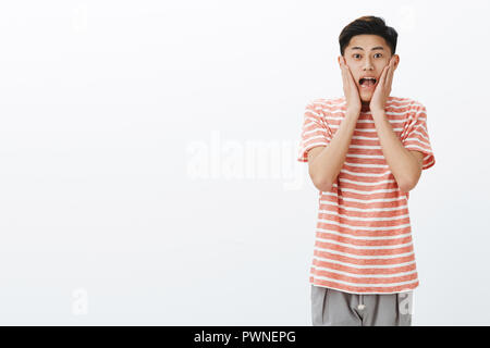 Portrait of impressed and surprised excited young asian male student screaming from amazement and joy pressing hands to cheeks and staring thrilled and astonished at camera on right side of copy space Stock Photo
