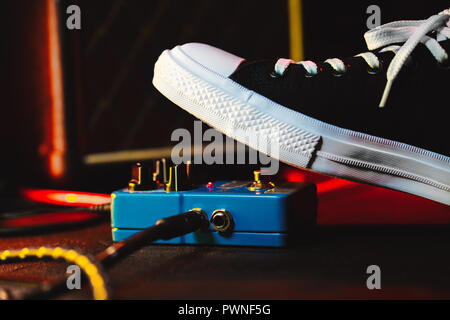 Close up of guitar player foot pressing pedal. Musician uses music effect loop machine. Man in trendy sneakers, his foot playing at stage during conce Stock Photo