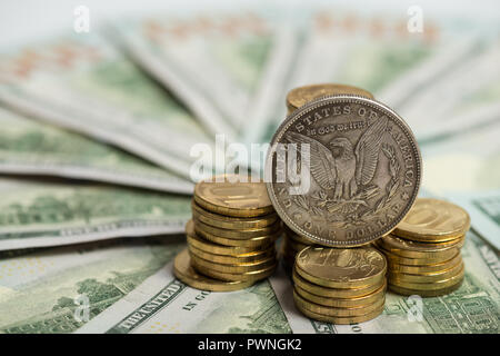 Investment concept - Old silver dollar coin on US Dollar bills and heap of golden coins Stock Photo