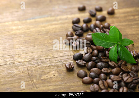 scattered roasted coffee beans and leaves on wooden background Stock Photo