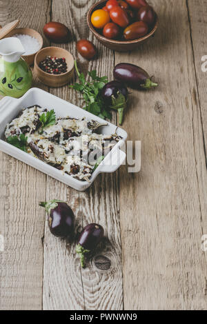 Stuffed eggplants with sun dried tomatoes and mozzarella cheese in ceramic dish on rustic wooden table Stock Photo