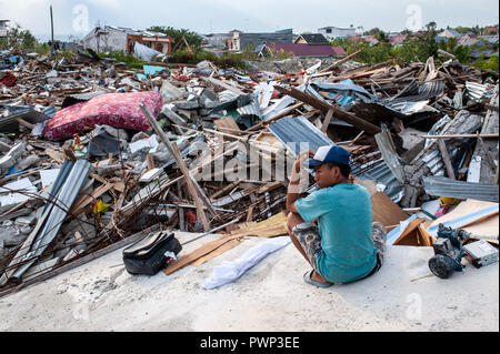 Sigi, Indonesia. 17th Oct, 2018. A resident is seen sited next to the ruins of buildings that were destroyed by the earthquake. A deadly earthquake measuring 7.5 magnitude and the tsunami wave caused by it has destroyed the city of Palu and much of the area in Central Sulawesi. According to the officials, death toll from devastating quake and tsunami rises to 2088, around 5000 people in hospitals are seriously injured and some 62,000 people have been displaced. Credit: SOPA Images Limited/Alamy Live News Stock Photo