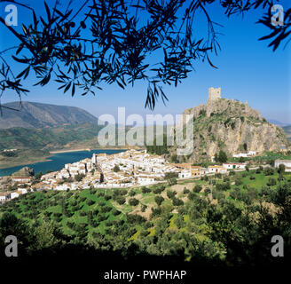 View over white town of Zahara de la Sierra with lake and castle atop rocky outcrop with olive groves beneath in afternoon sun Stock Photo