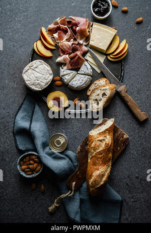 Cheese and ham plate with parmesan, camamber, goat cheese, ham, baguette and snacks. Overhead view, dark background Stock Photo