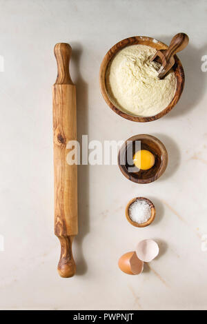 Ingredients for homemade italian pasta ravioli cooking semolina flour, egg yolk, sea salt with olive wood utensils bowls, scoop and rolling pin over w Stock Photo