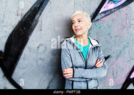 Senior Woman Relax After Running, Leaning On Wall. Short-Gray Hair, Sports Clothes , Looking At The Side Stock Photo