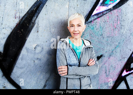 Senior Woman Relax After Running, Leaning On Wall. Short-Gray Hair, Sports Clothes , Looking At The Camera