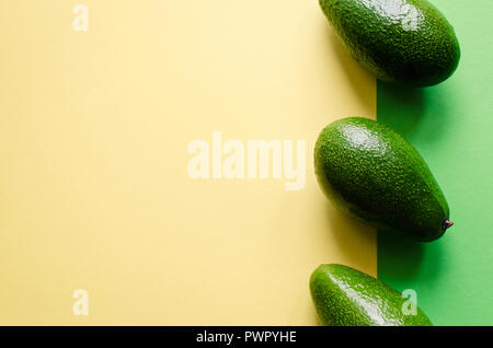 Organic avocado on color yellow and green background. Pop art design, creative summer food concept. Green avocadoes pattern in minimal flat lay style. Stock Photo