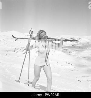 Winter in the 1940s. A young blonde swedish woman is carrying her skis on her shoulder, walking in the deep snow on a mountain top. She is wearing a swimsuit and enjoys the sunny day. Sweden 1940s. Photo Kristoffersson ref H139-6 Stock Photo