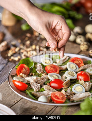 Female hand puts walnuts to the plate of freshly cooked salad from natural ingredients on a wooden table. Healthy diet eat. Stock Photo