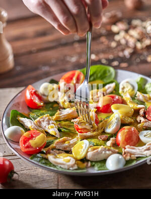Woman hand holds a fork with freshly prepared dietary vegetarian salad with natural organic vegetables on a wooden table. Stock Photo