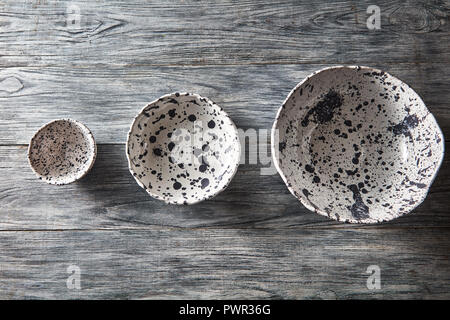 Ceramic bowls of different sizes are empty on a gray wooden background. Flat lay of porcelain dishes handmade. Stock Photo