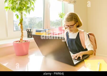 Young hacker little girl in glasses with a school backpack working at the computer, laptop. Stock Photo