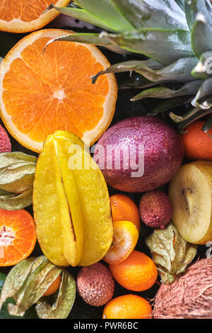 Natural organic background from exotic fruits carambola, half of orange, passion fruit, pineapple leaf in the drops water. Close-up. Stock Photo