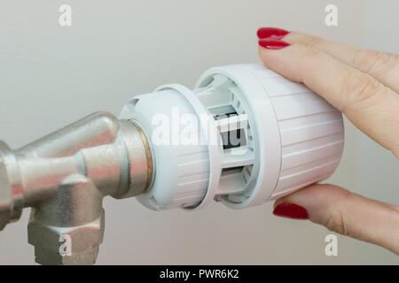 Heating radiator in an apartment. The female hand on the thermostat regulates the temperature Stock Photo