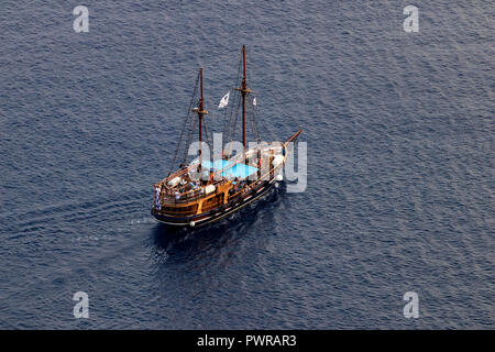 Luxury two-masted tourist boat sails out from Santorini island, Greece, August 2018, aerial view. Stock Photo