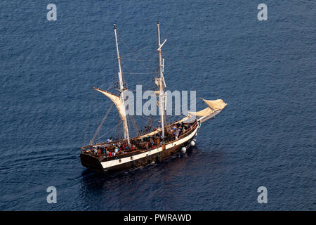 Luxury two-masted tourist boat sails out from Santorini island, Greece, August 2018. Aerial view. Stock Photo