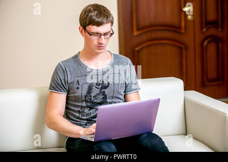 Concentrated young man with glasses working on a laptop in a home office. Pensively scans the text on the display. front view Stock Photo