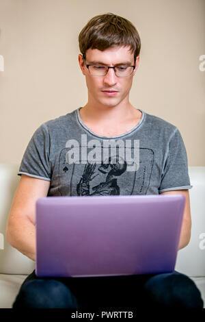 Concentrated young man with glasses working on a laptop in a home office. front view Stock Photo