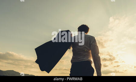 Retro image of successful young businessman standing under glorious evening sky confidently swishing his jacket over his shoulder. Stock Photo