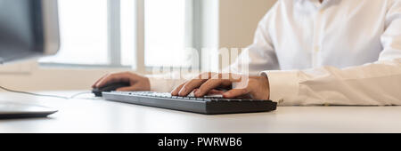 Wide view image of businessman sitting at office desk using and typing on computer keyboard. Stock Photo