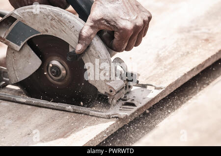 Hand of a carpenter using a circular saw to cut a wooden plank. Tool used to saw wood. Carpentry tool. Electric saw, circular blade. Stock Photo