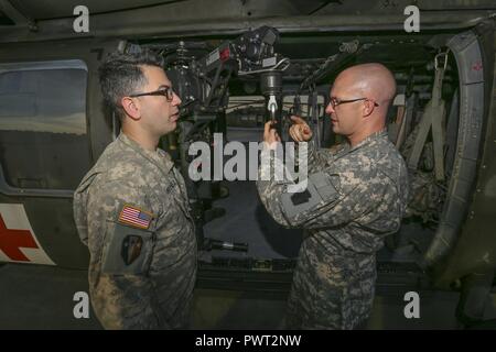 U.S. Army Sgt. Timothy Witts, right, a Black Hawk crew chief, briefs Chief Warrant Officer 2 Oscar Martinez, a Black Hawk pilot, on the hoist system during joint training for New Jersey Task Force One at Joint Base McGuire-Dix-Lakehurst, N.J., June 28, 2017. The primary mission of New Jersey Task Force One is to provide advanced technical search and rescue capabilities to victims trapped or entombed in structurally collapsed buildings. Task Force One is made up of New Jersey National Guard Soldiers and Airmen, as well as civilians. Stock Photo