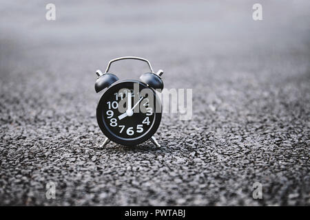 Black alarm clock with white number on the dark rough street background texture with copy space. Stock Photo