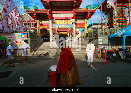 A Thai Buddhist monk passes the Taoist Jui Tui Temple in Phuket Town, Phuket, Thailand, on his early morning alms round, the alms bowl in his hands Stock Photo