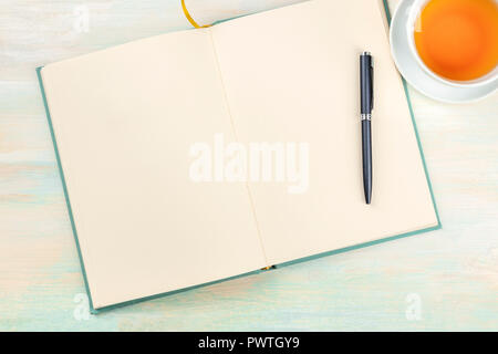 A photo of an open journal with a pen and a cup of tea, shot from the top, on a light background with a place for text Stock Photo