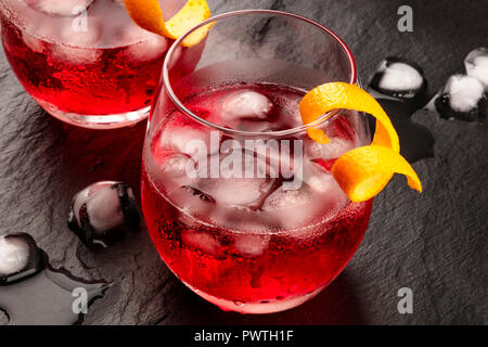 A photo of two vibrant cocktails with campari and orange twist garnishes, with ice cubes on a black background, with copy space Stock Photo