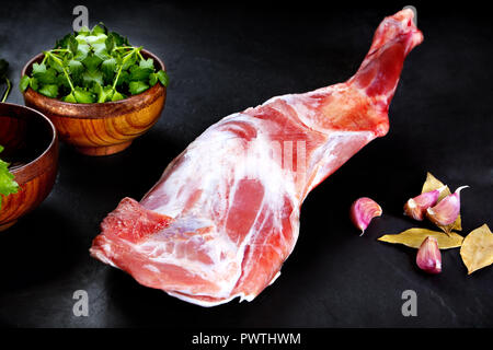 Fresh and raw meat. Leg of lamb uncooked , ready to grill and barbecue on black slate background Stock Photo