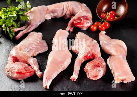 Feeding. Fresh and raw meat for butcher shop. Rabbit in pieces ready to cook on black background of black slate Stock Photo