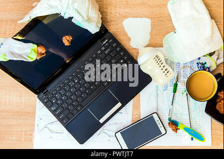 A concept image for having baby and working from home. Messy workplace, diaper, porridge for a child on screen, spilled milk. Stock Photo