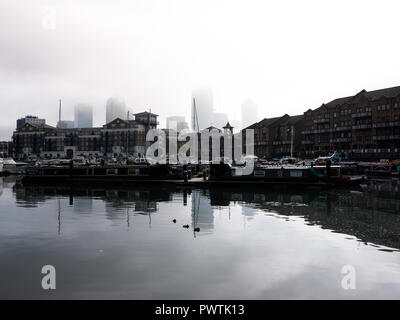 Low cloud hides the top of the tall buildings at Canary Wharf as seen from Limehouse Basin in East London Stock Photo