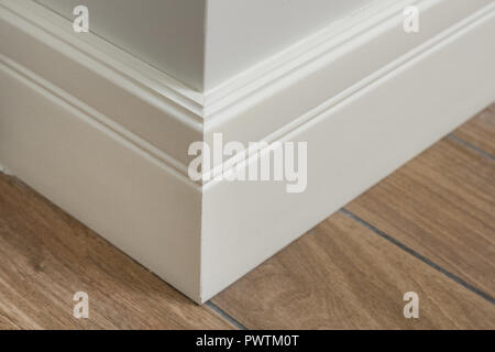 Molding in the interior, baseboard corner. Light matte wall with tiles immitating hardwood flooring. Stock Photo
