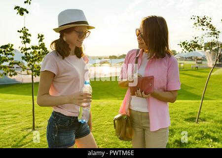 Communication of the parent and adolescent. Mother talks to her daughter teenager, takes out purse with money from her bag. Background green gas, recr Stock Photo