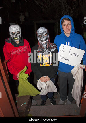 Three young teenage boys in monster skull masks & ceiling lover costumes out for an evening of Halloween tricks or treats.  St Paul Minnesota MN USA Stock Photo