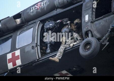 U.S. Army National Guard Sgt. Timothy Witts, a UH-60 Black Hawk helicopter crew chief, scans the area before lowering a hoist during joint training for New Jersey Task Force One at Joint Base McGuire-Dix-Lakehurst, N.J., June 28, 2017. The primary mission of New Jersey Task Force One is to provide advanced technical search and rescue capabilities to victims trapped or entombed in structurally collapsed buildings. Stock Photo