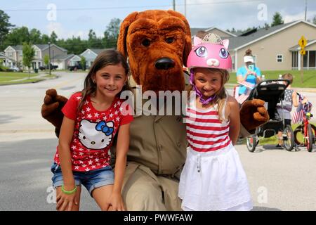 Ashlyn, 8, left, and Adelyn, 5, pose with McGruff the Crime Dog during the first Independence Day Youth Parade at Marine Corps Air Station Cherry Point, N.C., July 4, 2017. Nearly 100 members of the Cherry Point community joined in on the red, white and blue parade. The mile-long bike parade was organized by housing resident Caitlin Chemelewski as a patriotic and fun event for the kids, and to bring the MCAS Cherry Point community together on Independence Day. Stock Photo