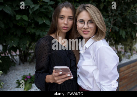 Two young women are standing on the street and using a smartphone. Stock Photo