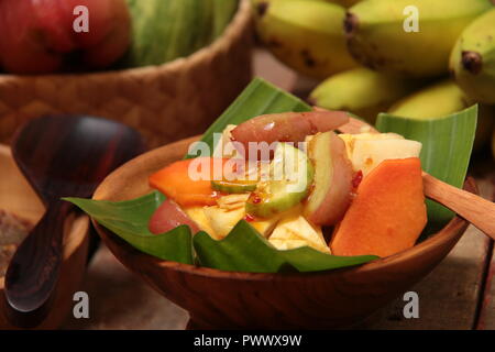 Rujak Buah, the Indonesian fruit salad with spicy coconut sugar dressing. Plated on a shallow wooden bowl lined with banana leaf, Stock Photo