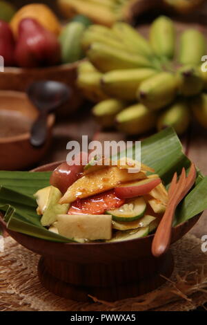 Rujak Buah, the Indonesian fruit salad with spicy coconut sugar dressing. Plated on a shallow wooden bowl lined with banana leaf, Stock Photo