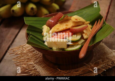 Rujak Buah, the Indonesian fruit salad with spicy coconut sugar dressing. Plated on a shallow wooden bowl lined with banana leaf, Stock Photo