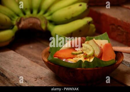 Rujak Buah, the Indonesian fruit salad with spicy coconut sugar dressing. Plated on a shallow wooden bowl lined with banana leaf, Stock Photo