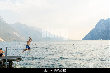 Handsome funny attractive man having fun jumping into the water in lago di garda in Italy in summer holidays Fun vacations travel around Europe. Stock Photo
