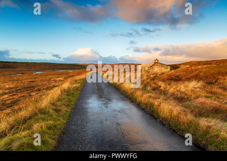 A single track road over a peat bog and past a shieling hut near Stornoway on the Isle of Lewis in the Outer Hebrides in Scotland Stock Photo