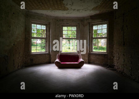 Interior view of a dark room with red sofa in an abandoned hospital in Germany. Stock Photo