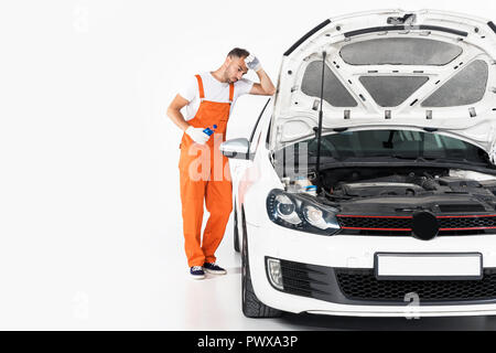 tired auto mechanic holding bottle of water and leaning on car on white Stock Photo